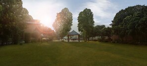 A park with a gazebo, trees, and a building in the background. - Voco Jim Corbett (Ramnagar)