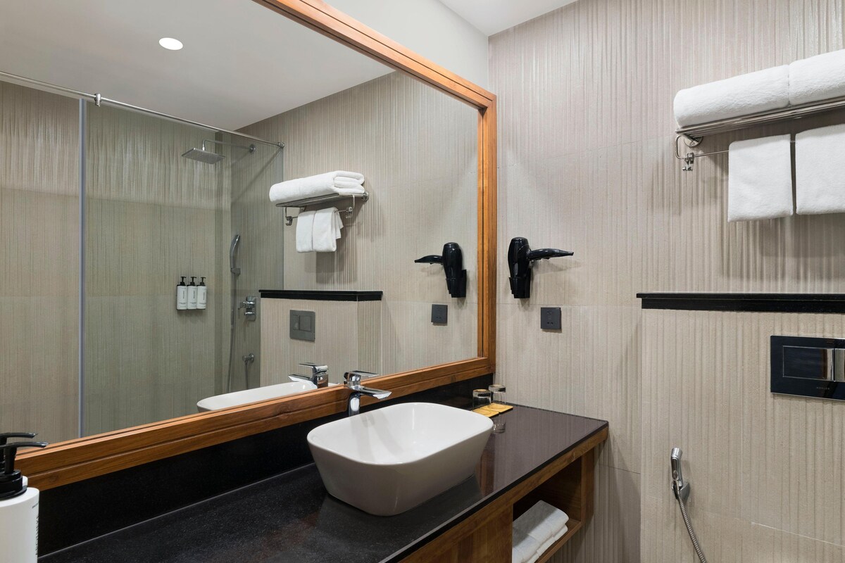 A modern bathroom with a large mirror, a sink, a shower, and towel racks.