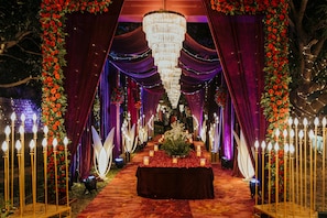 An outdoor wedding aisle with a red carpet, floral decorations, and a chandelier. - Voco Jim Corbett (Ramnagar)