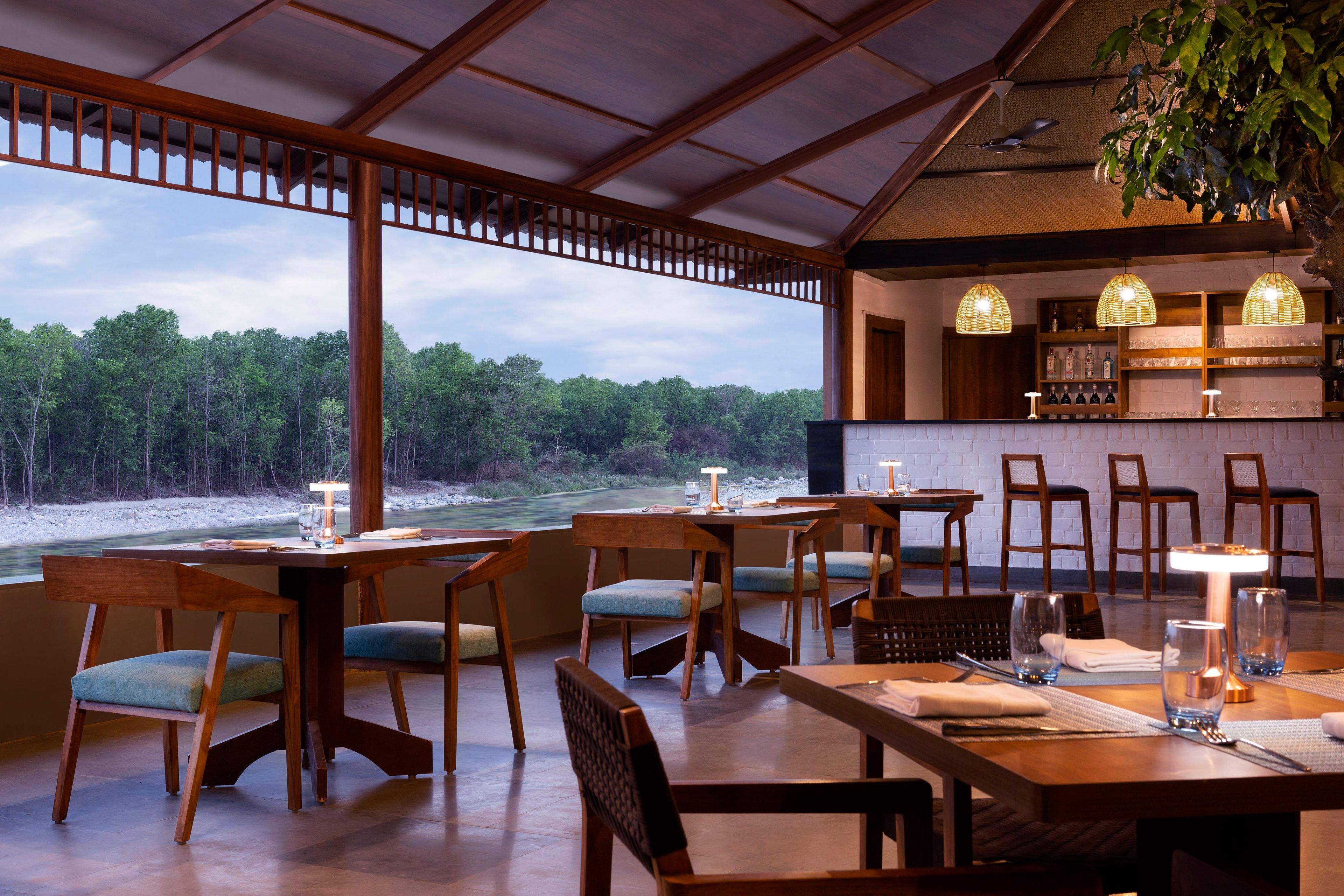 Un restaurant doté de meubles en bois, offrant une vue sur la forêt, et comprenant un espace bar avec des bouteilles exposées.