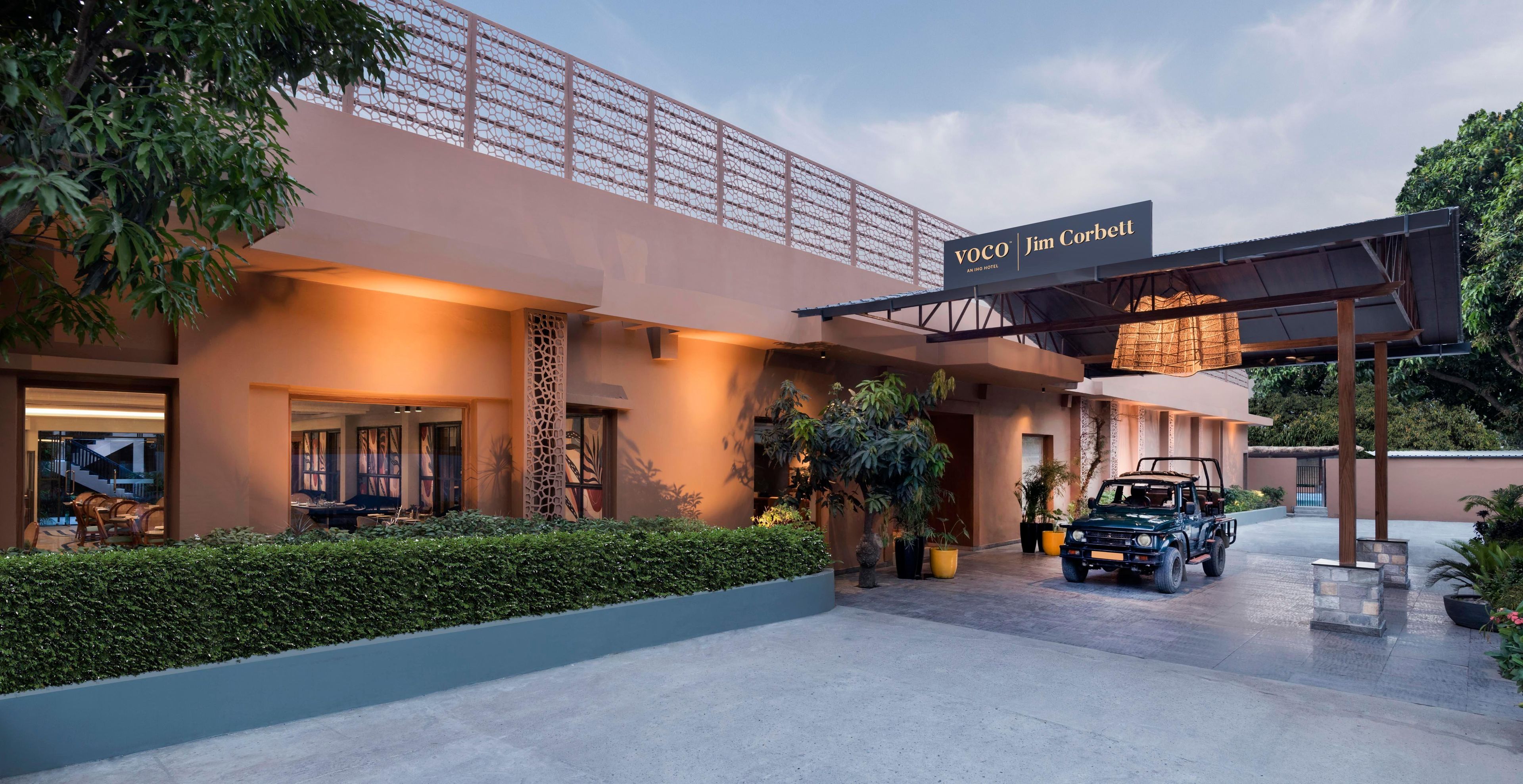 A hotel entrance with a covered driveway, a sign reading "VOCO Jim Corbett", and a vehicle parked in front.