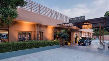 A hotel entrance with a covered driveway, a sign reading "VOCO Jim Corbett", and a vehicle parked in front.