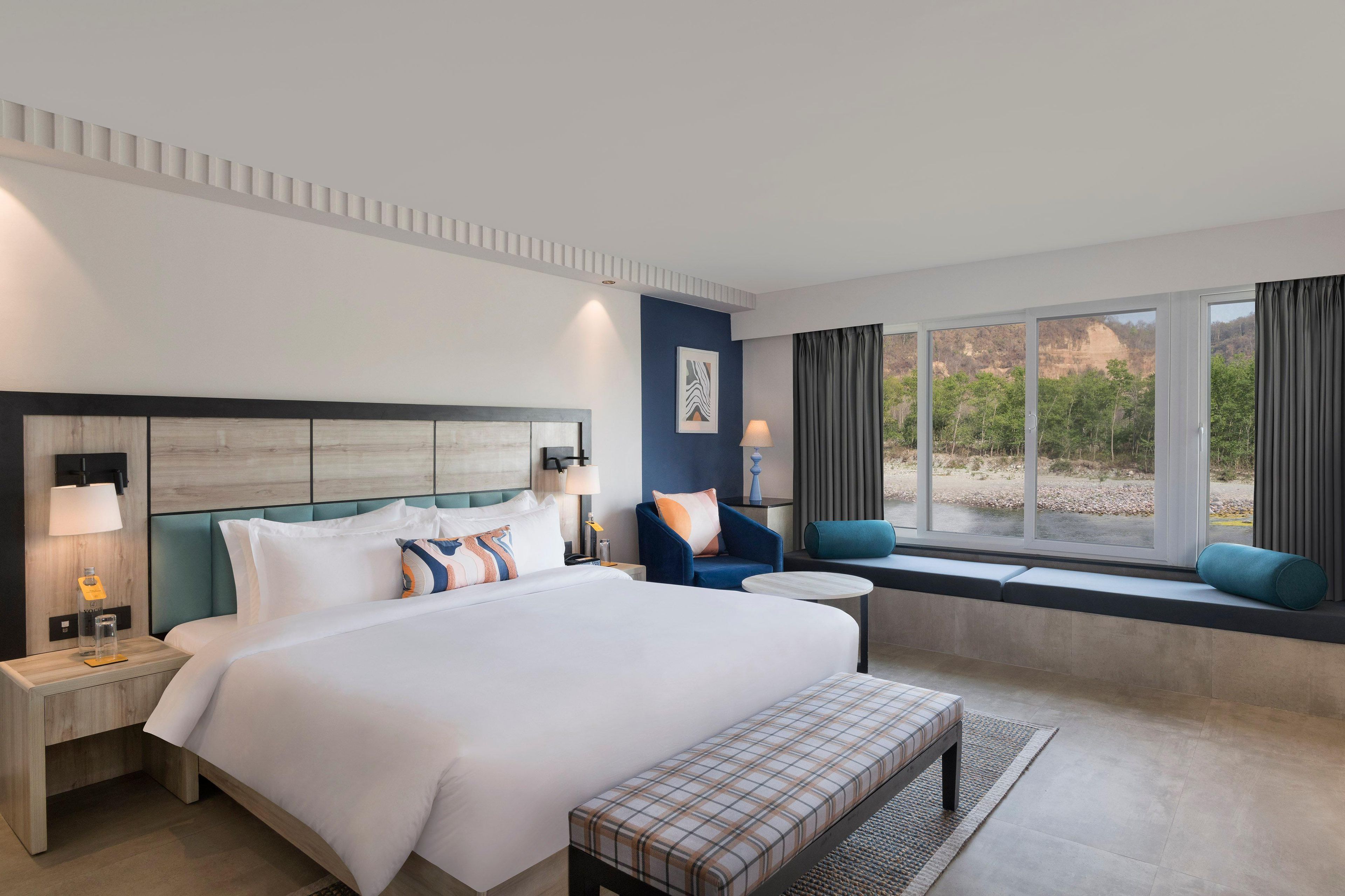 Une chambre d’hôtel moderne dotée d’un grand lit, d’un coin salon près de la fenêtre et offrant une vue sur l’extérieur.