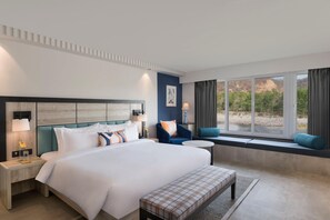 Une chambre d’hôtel moderne dotée d’un grand lit, d’un coin salon près de la fenêtre et offrant une vue sur l’extérieur.