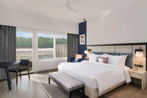 Une chambre d’hôtel moderne, dotée d’un grand lit, d’un bureau et d’une chaise. Les fenêtres offrent une vue sur l’extérieur.