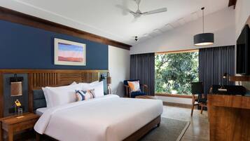 Une chambre d’hôtel avec un grand lit, un bureau, une chaise, un ventilateur de plafond et une fenêtre avec des rideaux.