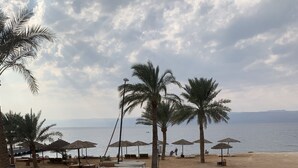 A beach with palm trees, umbrellas, and a sandy area. - Rose beach chalet  (Aqaba)