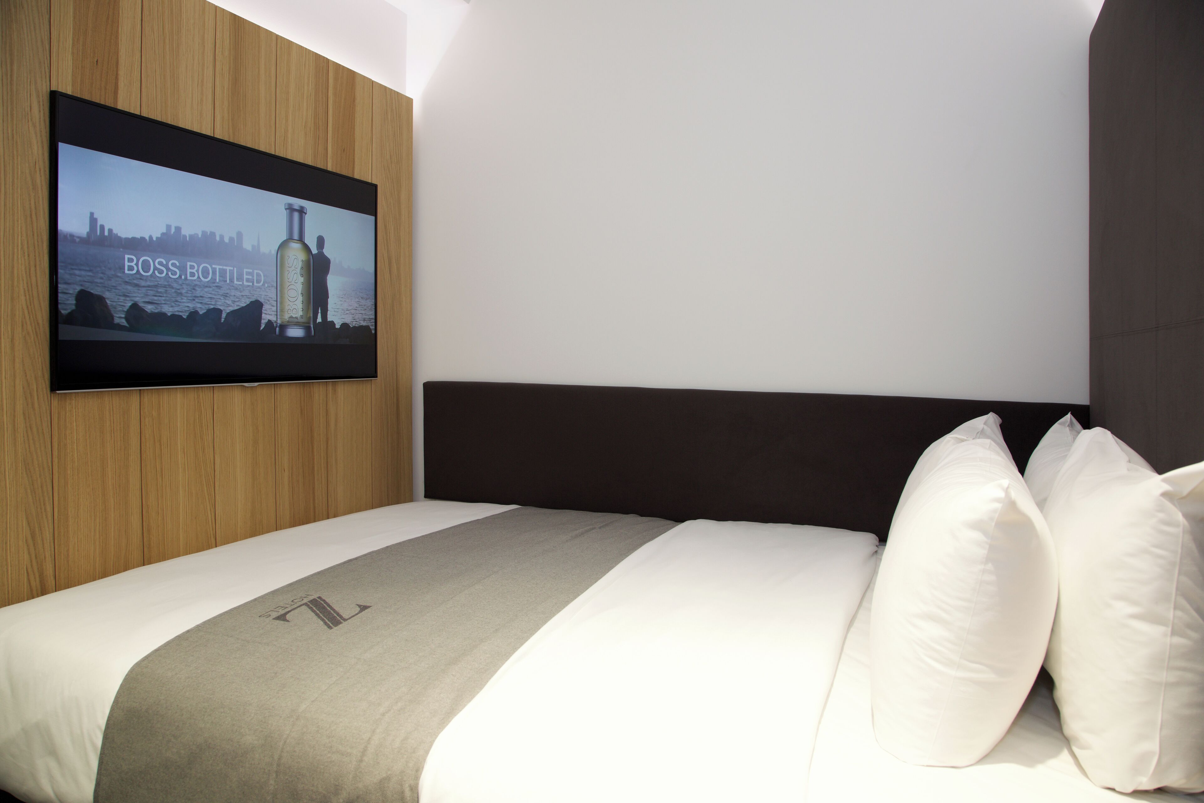 A hotel room with a bed, a television mounted on the wall, and a cityscape view on the screen.