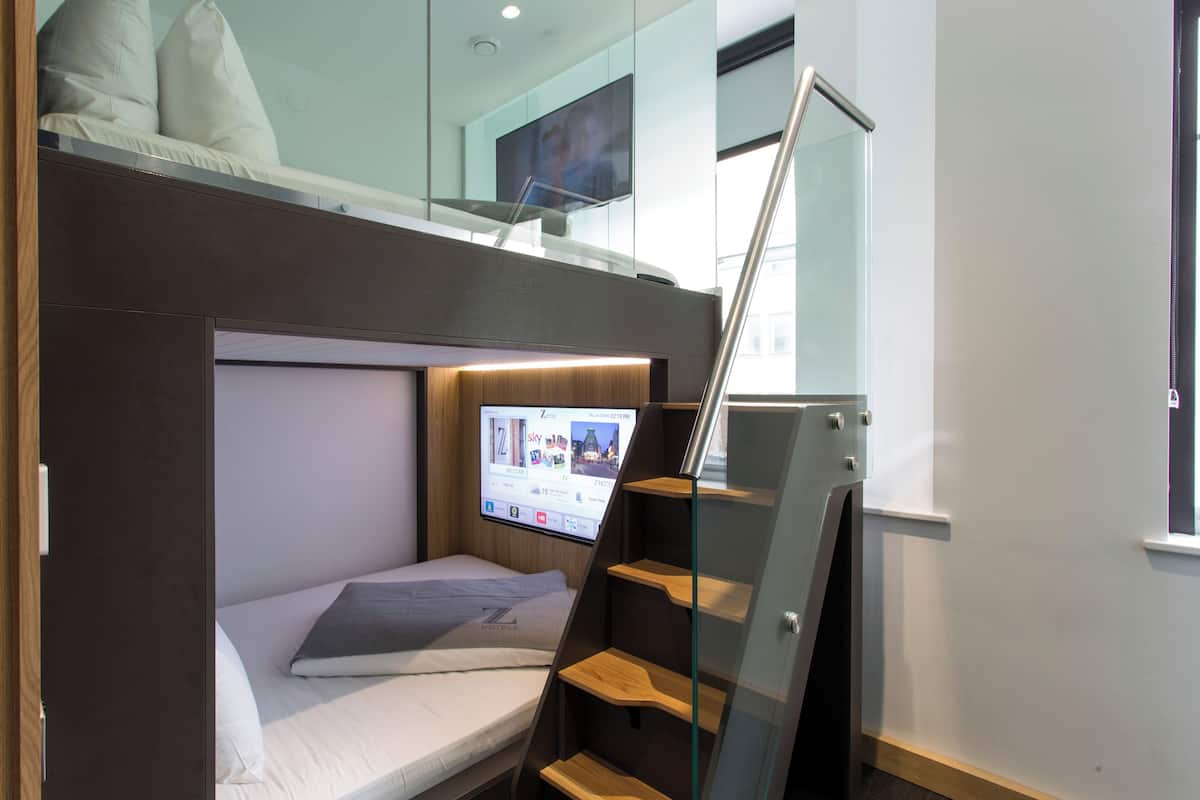 A compact hotel room with a bunk bed, a small desk with a computer, and a TV mounted on the wall.