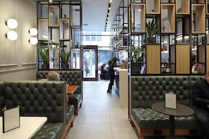 A modern interior with green upholstered booths, a central bar area, and shelves with plants and books. - The Z Hotel City (London)