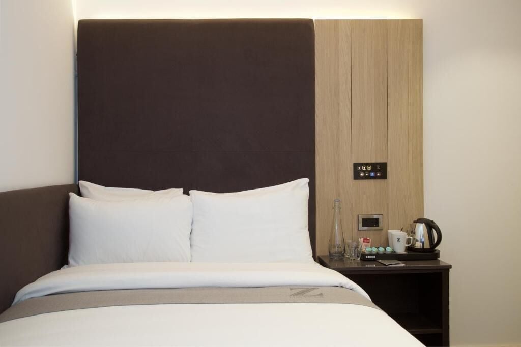 Ein Hotelzimmer mit Bett, Nachttisch, Kaffeemaschine und Bedienfeld.