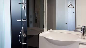 Un bagno moderno con cabina doccia in vetro, un lavandino bianco e uno specchio con un appendiabiti in legno.