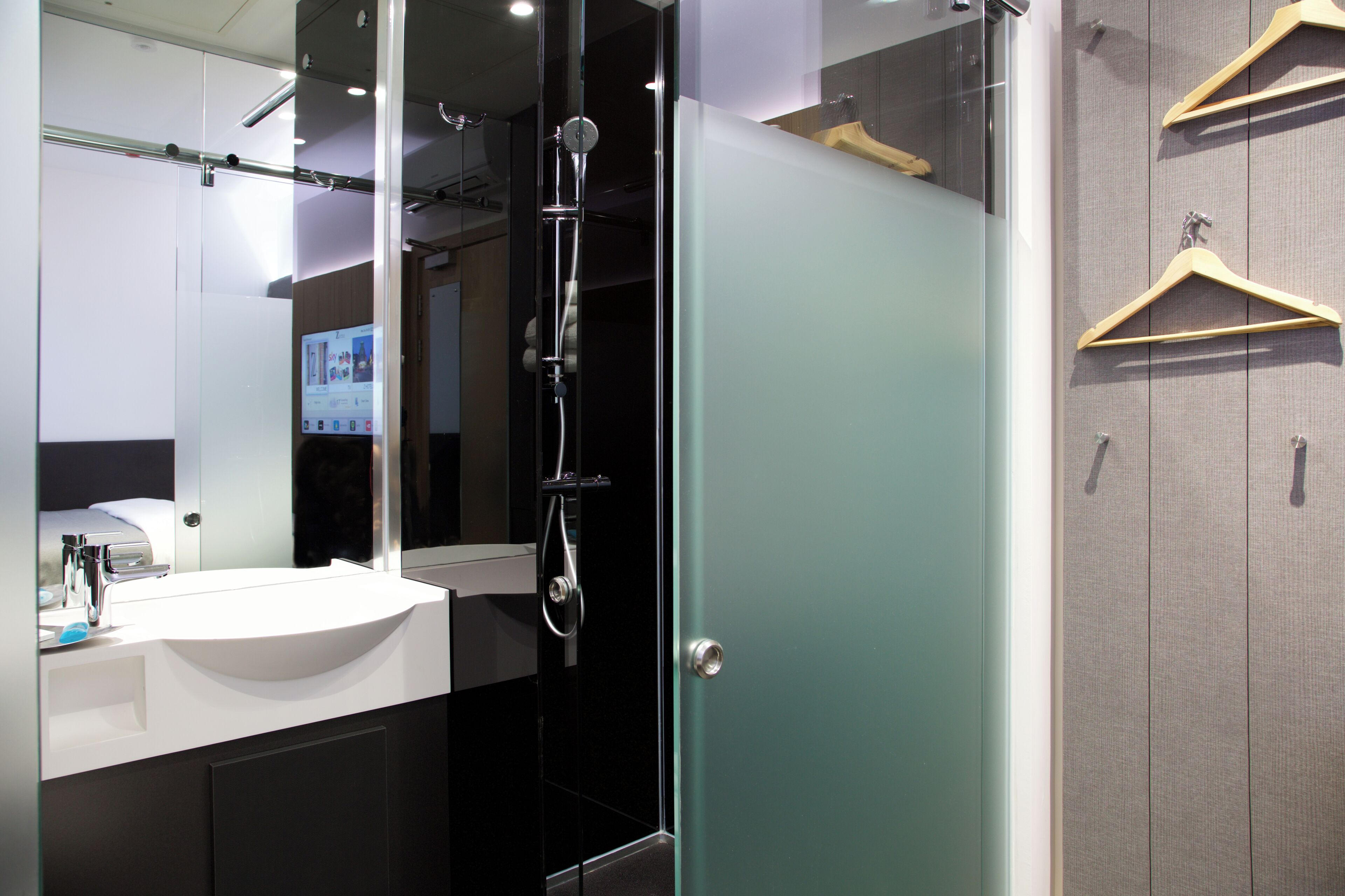 A modern bathroom with a glass shower enclosure, a white sink, and wooden hangers on the wall.