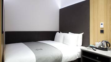Een moderne hotelkamer met een groot bed, een nachtkastje met waterkoker en een bedieningspaneel aan de muur.