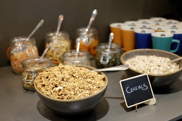 A breakfast buffet with various cereal options in bowls and jars, a sign indicating 'Cereals', and a selection of mugs in the background. - The Z Hotel City (London)