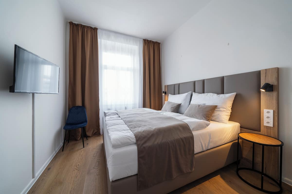 A modern hotel room with a large bed, a flat-screen TV mounted on the wall, a small round table, and a chair.