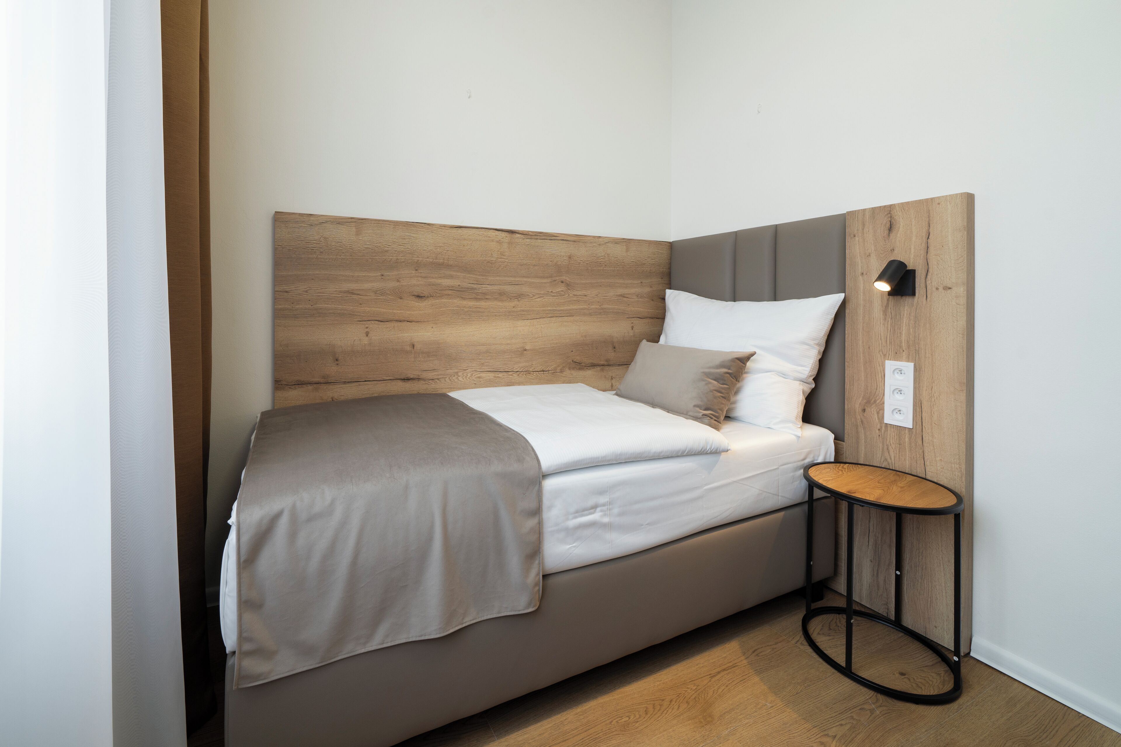 A single bed with a wooden headboard, a bedside table, and a wall-mounted light fixture.