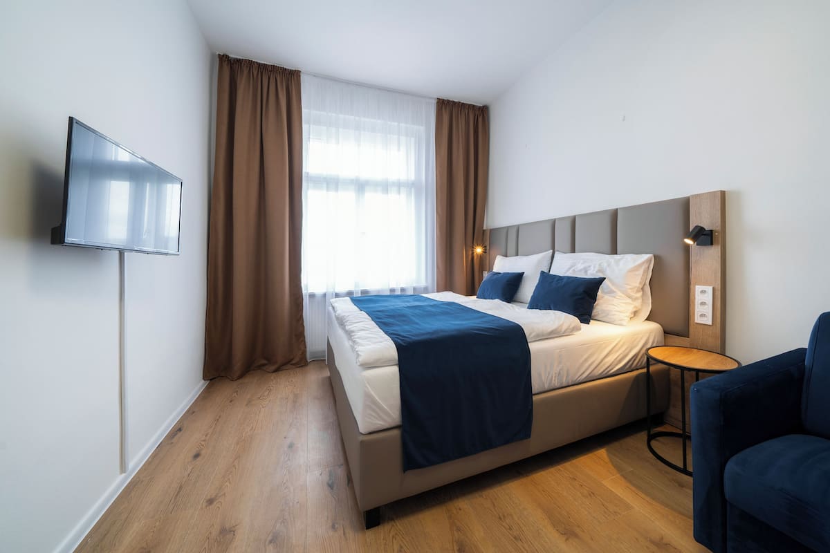 A modern hotel room with a bed, a TV, a bedside table, and a chair.