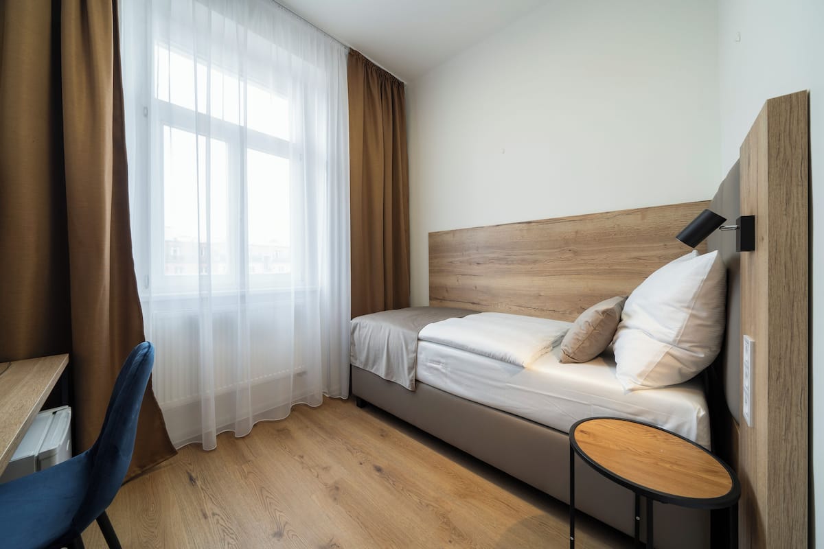 A bedroom with a wooden headboard, a bed with white bedding, a small round table, and a chair.