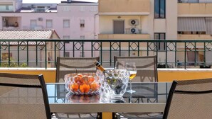 A balcony with a table set for two, featuring a bowl of oranges, a bottle of champagne, and a glass of wine.
