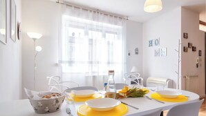 A dining area with a table set for two, featuring white plates, yellow placemats, and a centerpiece of flowers.