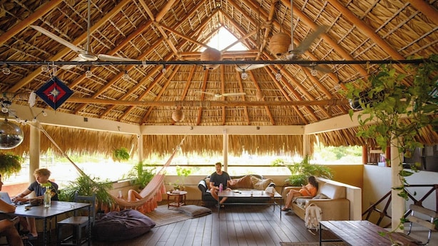 A spacious indoor area with a thatched roof, wooden flooring, and comfortable seating arrangements. - Puerto Dreams H (Puerto Escondido)