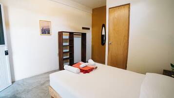 A bedroom with a bed, a wooden wardrobe, a mirror, and a framed picture on the wall.