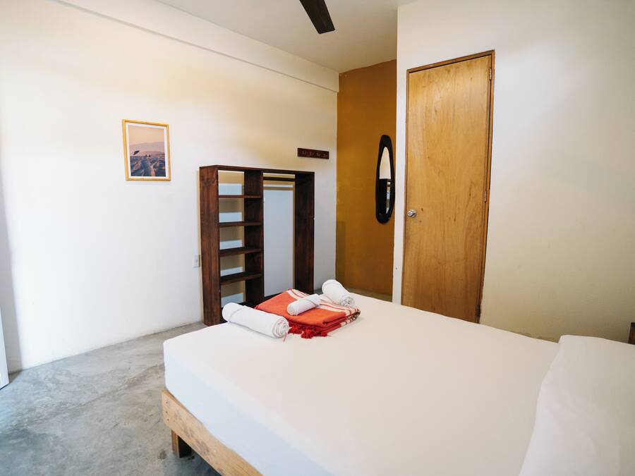 A bedroom with a bed, a wooden wardrobe, a mirror, and a framed picture on the wall.