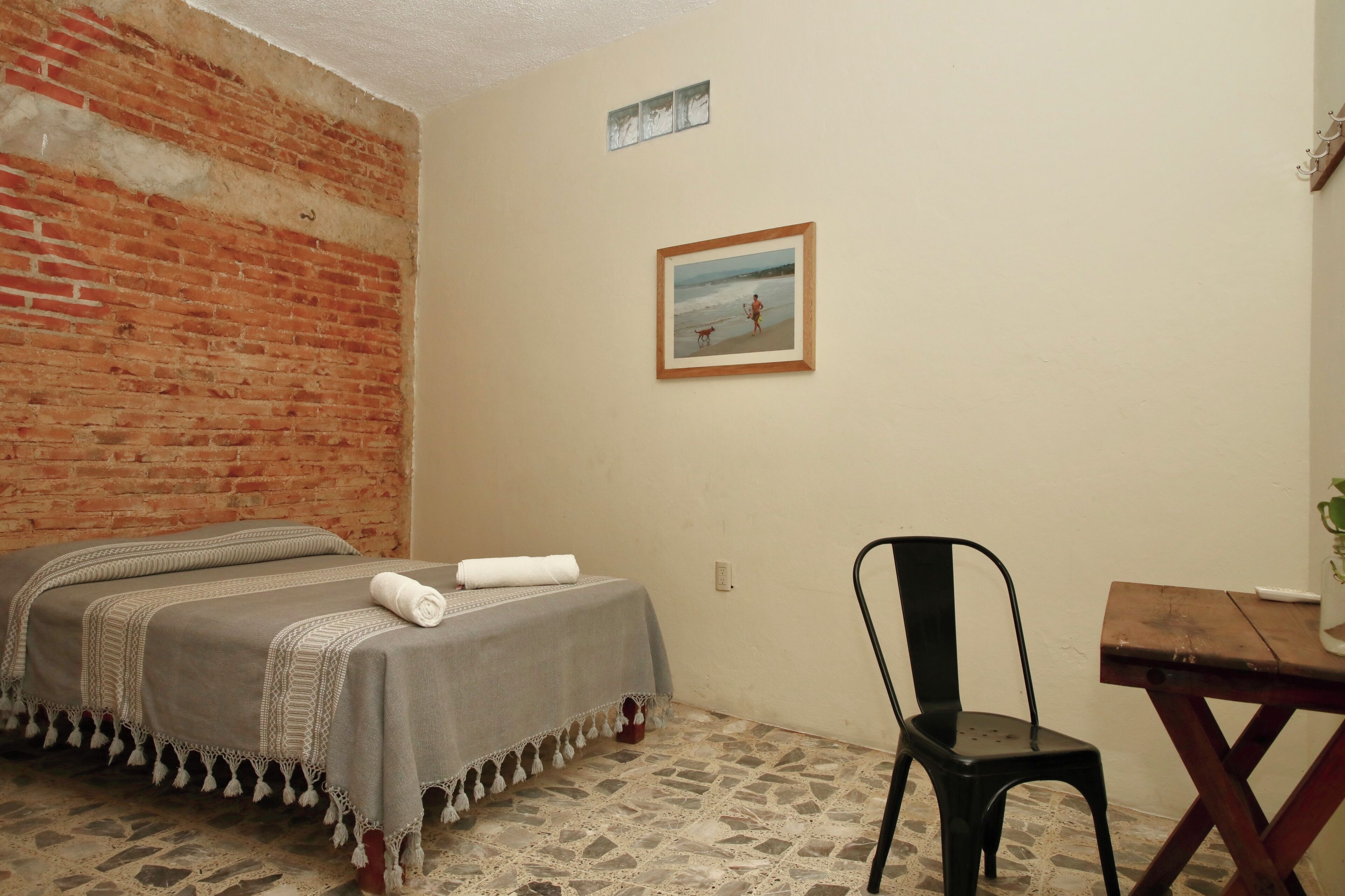 Una habitación con una cama, una silla, una mesita y un cuadro en la pared.