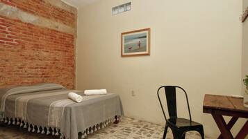 Una habitación con una cama, una silla, una mesita y un cuadro en la pared.