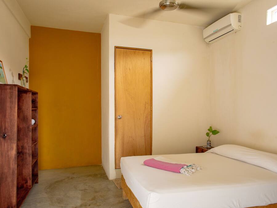 Quarto com cama, guarda-roupa de madeira, porta e ar condicionado.