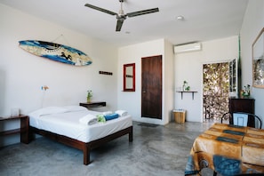Un dormitorio con cama, ventilador de techo, puerta de madera y vistas al exterior.