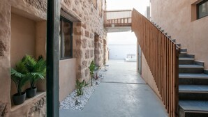 Un estrecho callejón con un sendero de concreto, plantas en macetas y una cerca de madera.