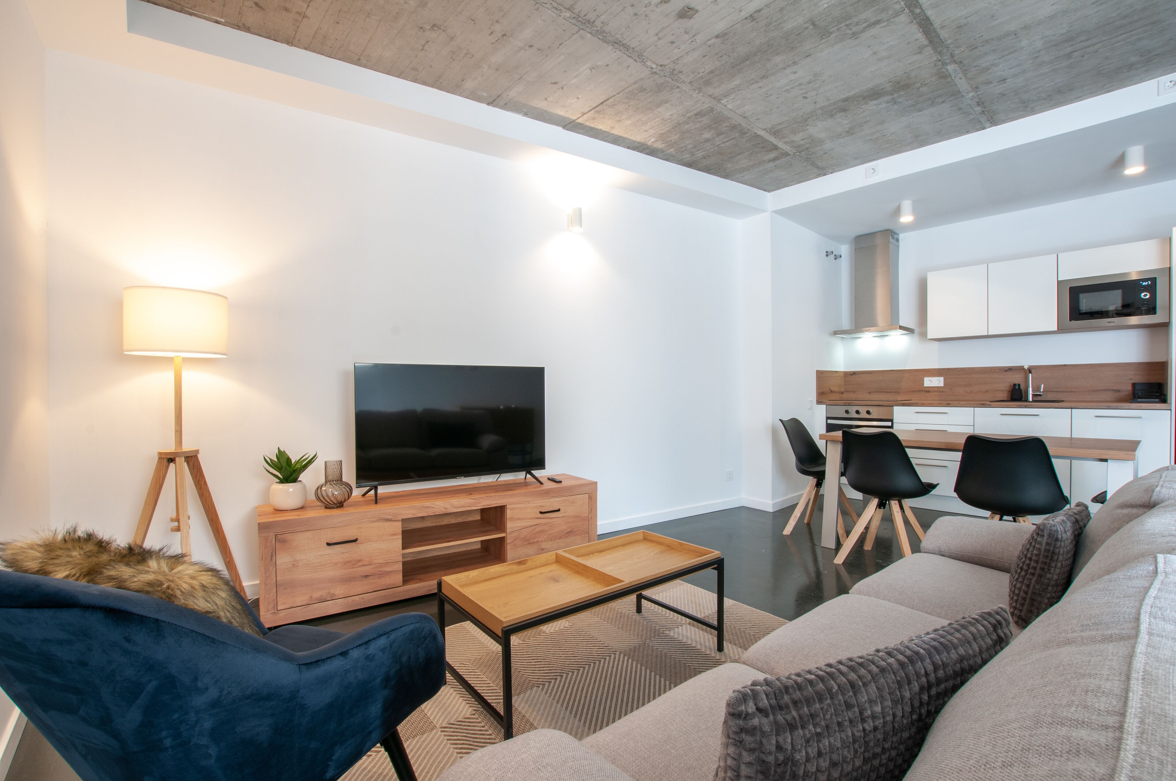 Een moderne woonkamer met een bank, een salontafel, een televisie en een eethoek met stoelen, met een keuken op de achtergrond.