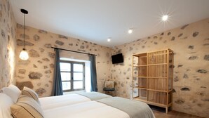 Une chambre avec deux lits, une bibliothèque en bois, une télévision et une fenêtre avec des rideaux.