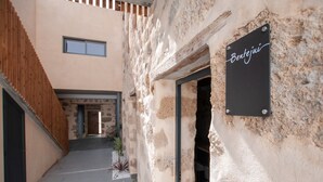 Une ruelle étroite mène à un bâtiment rustique doté d’une façade en pierre et d’une clôture en bois. Une enseigne noire portant l’inscription « Bentejui » est fixée au mur.