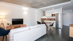 Un salon moderne doté d’un téléviseur à écran plat, d’un canapé blanc et d’un coin repas avec une table et des chaises en bois.