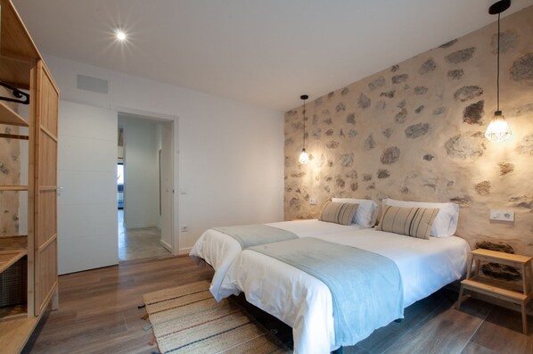 Ein Schlafzimmer mit zwei Betten, einem Holzschrank, einer Wand mit Steinmusterung und einem kleinen Tisch mit einer Lampe.