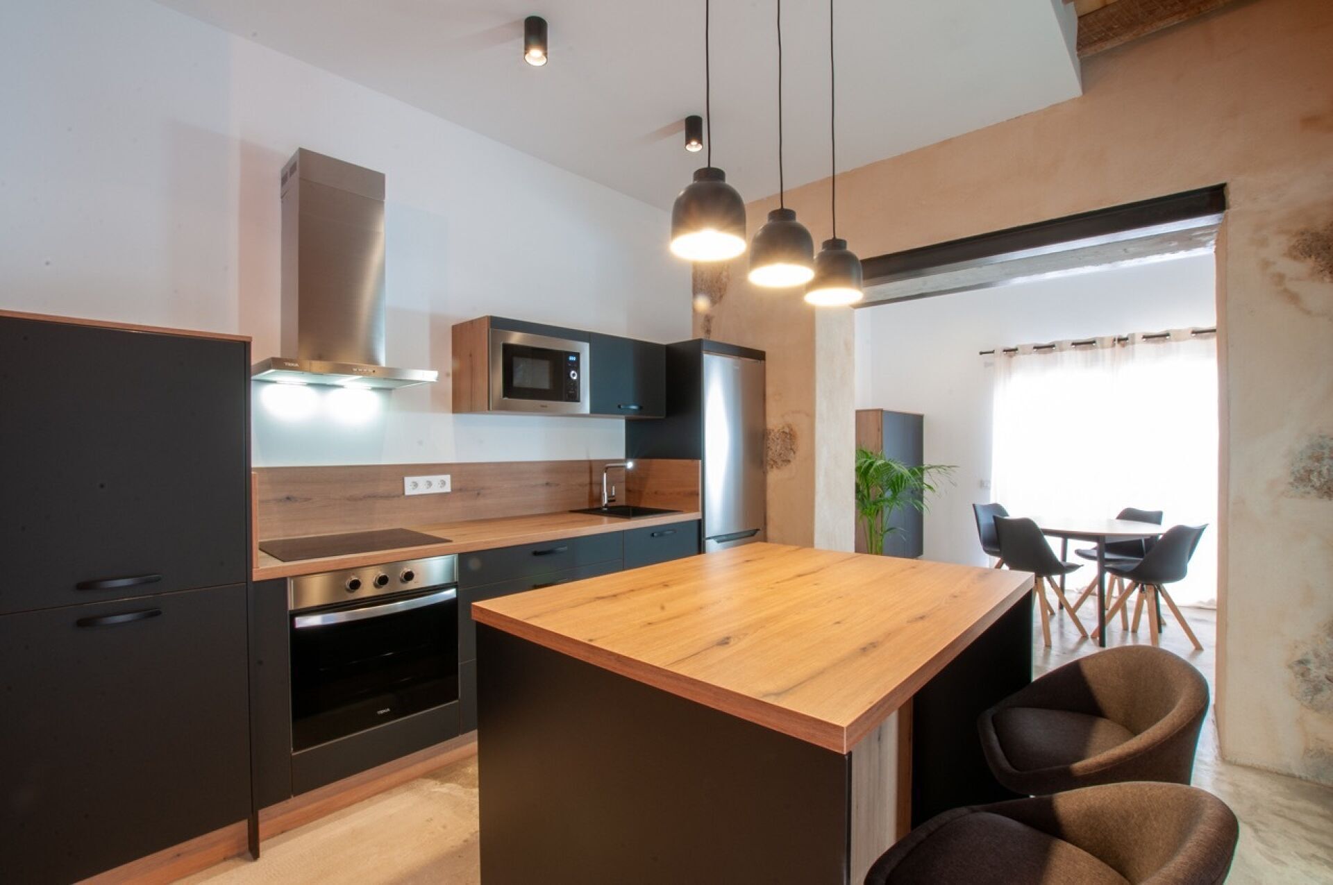 Une cuisine moderne dotée d’un îlot central, d’appareils électroménagers intégrés et de luminaires suspendus.