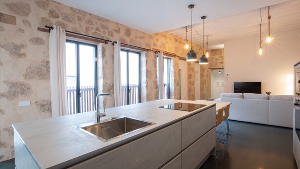 Una cocina moderna con una isla grande, electrodomésticos integrados y una zona de comedor con un sofá blanco.