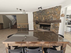Cozy dining area with a stone fireplace, glass-top table, and staircase leading to an upper level.