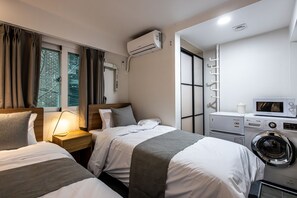 Une chambre d’hôtel avec deux lits, un lave-linge, un four à micro-ondes et une fenêtre avec des rideaux.
