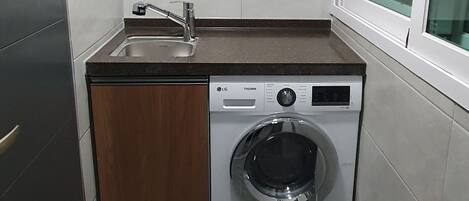 A compact kitchen with a built-in washing machine, a sink, and a window.
