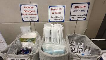 A hotel self-service station with labeled bins for laundry detergent, dental kit & razor, and an adapter. Instructions for using the laundry detergent and returning the adapter are provided.