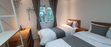 A bedroom with two beds, a desk, and a window with curtains.