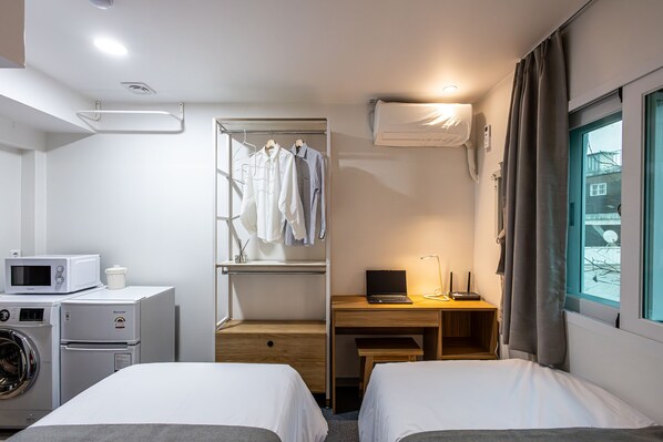 Une chambre d’hôtel avec un lit, un bureau avec un ordinateur portable, un lave-linge et un étendoir à linge.