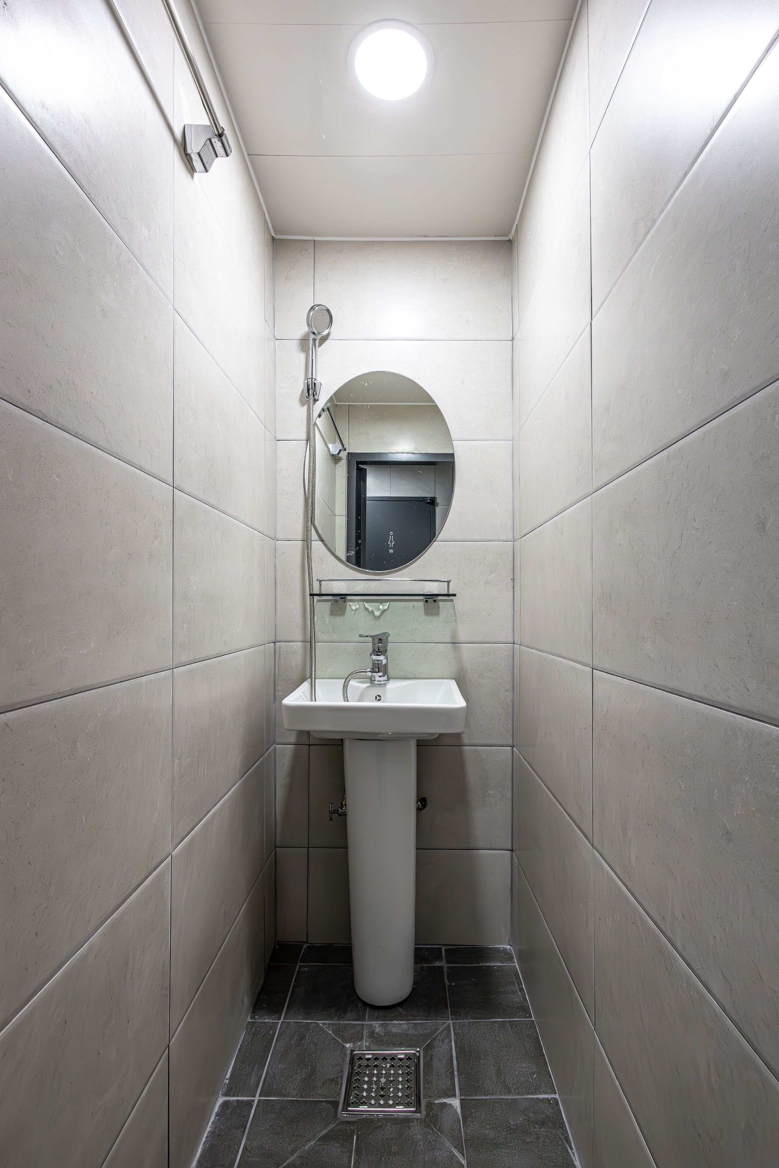 Un baño pequeño y moderno con lavamanos pedestal, un espejo redondo y ducha.