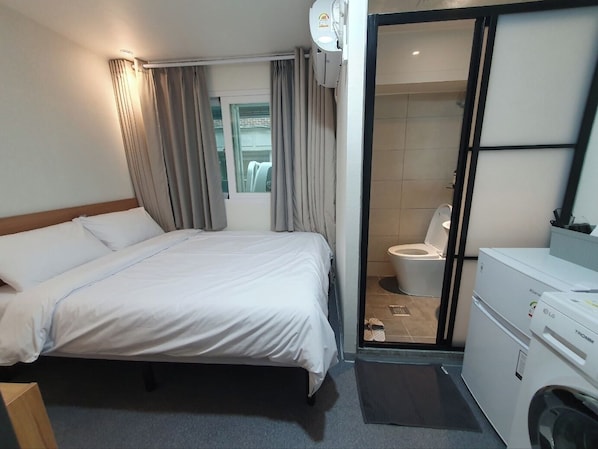 Habitación de hotel con cama, baño con inodoro y lavadora.