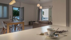 Un salon moderne avec un coin repas, de grandes fenêtres offrant une vue sur la mer et un design minimaliste.