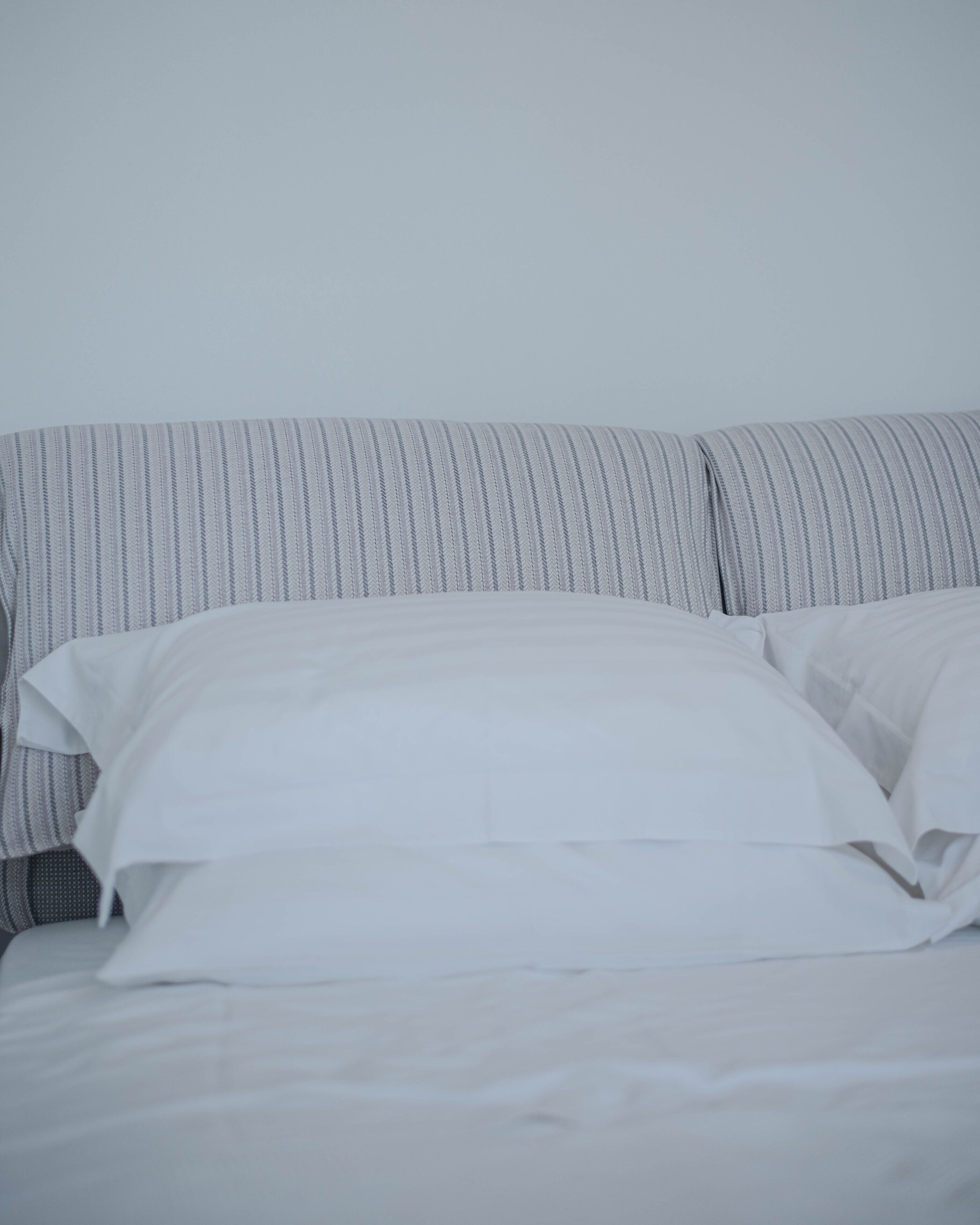 A bed with white linens and striped pillows against a plain wall.